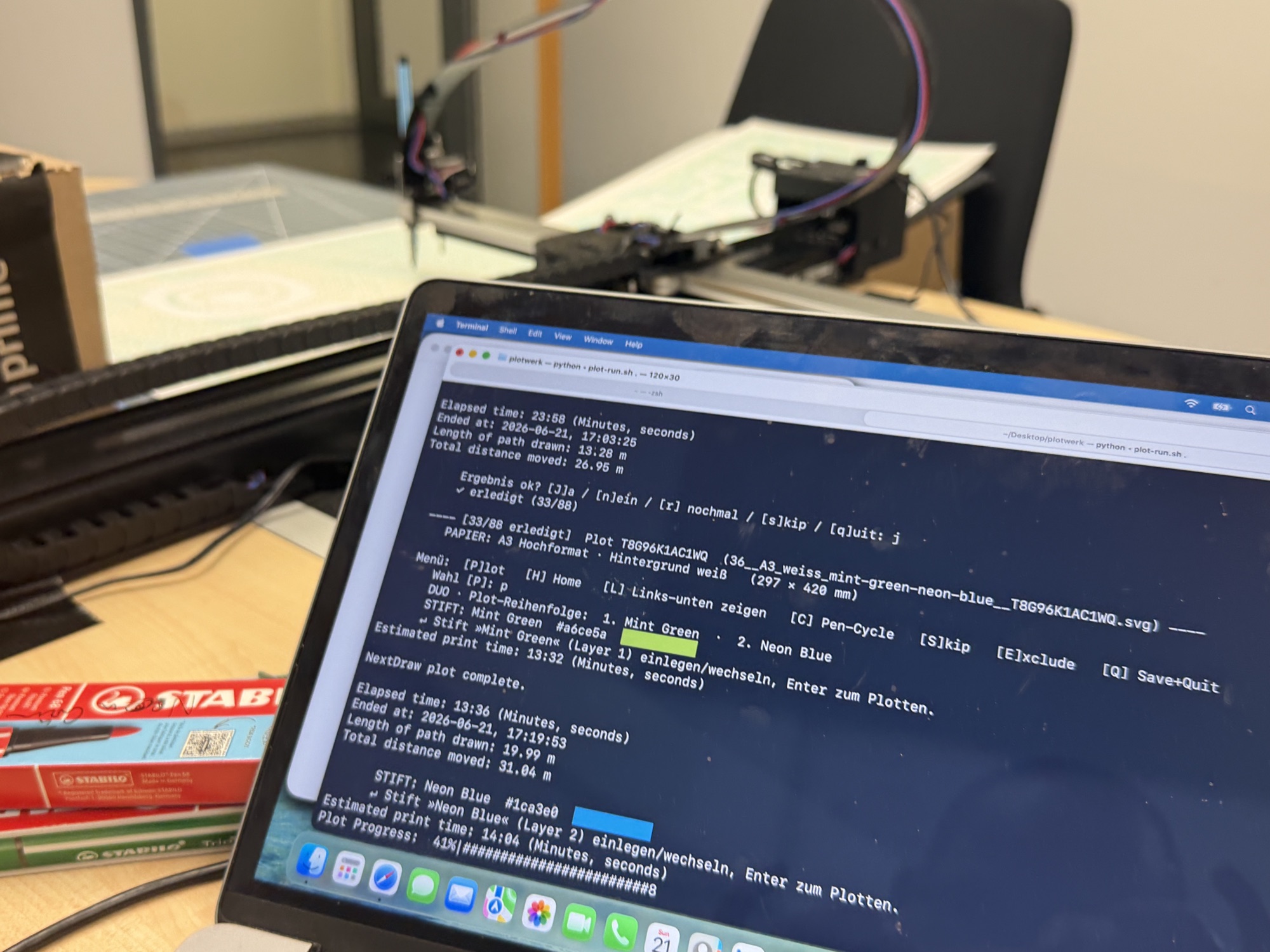Laptop mit dem selbstgebauten Plot-Treiber im Terminal: ein Menü mit Plot, Skip und Exclude, daneben ein Stiftkasten und der laufende Plotter im Hintergrund