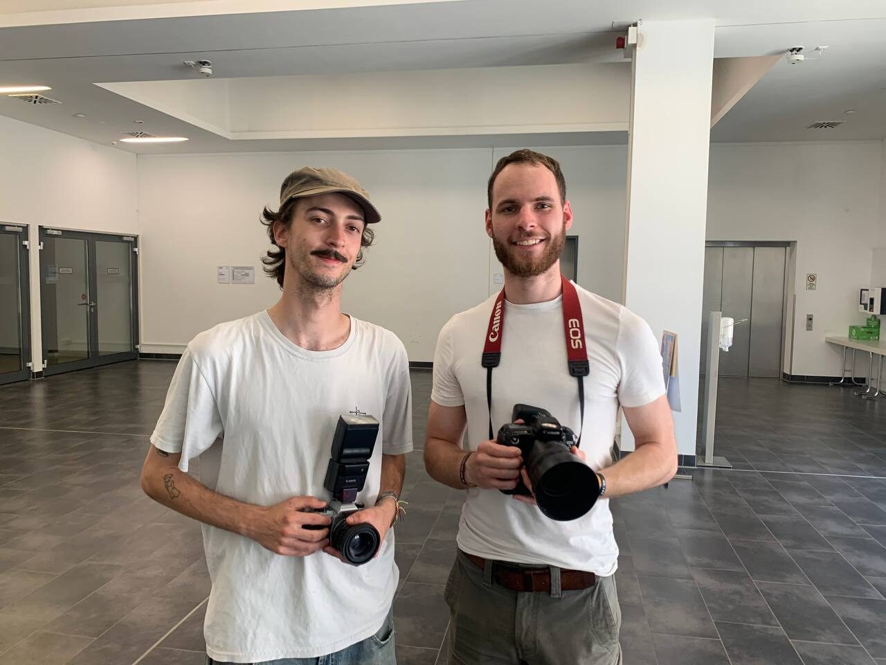 Zwei junge Männer mit analogen Kameras im Foyer der Universität: links Jonathan Friedrich mit Mütze und Aufsteckblitz, rechts Moritz Wiederhold mit einer Canon-EOS-Spiegelreflexkamera