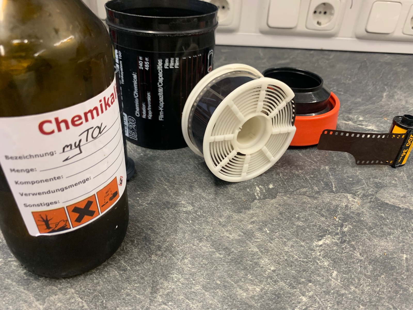 Entwicklungsdose, Filmspule, belichteter Kleinbildfilm und Chemikalienflasche auf dem Arbeitstisch