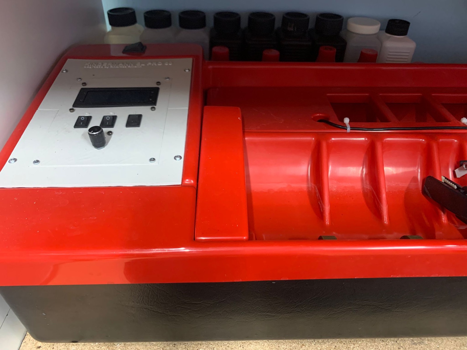 Die Rotationsmaschine: rotes Gehäuse mit selbst gebautem Bedienpanel aus LCD-Display, Schaltern und Drehencoder, im Hintergrund Chemikalienflaschen