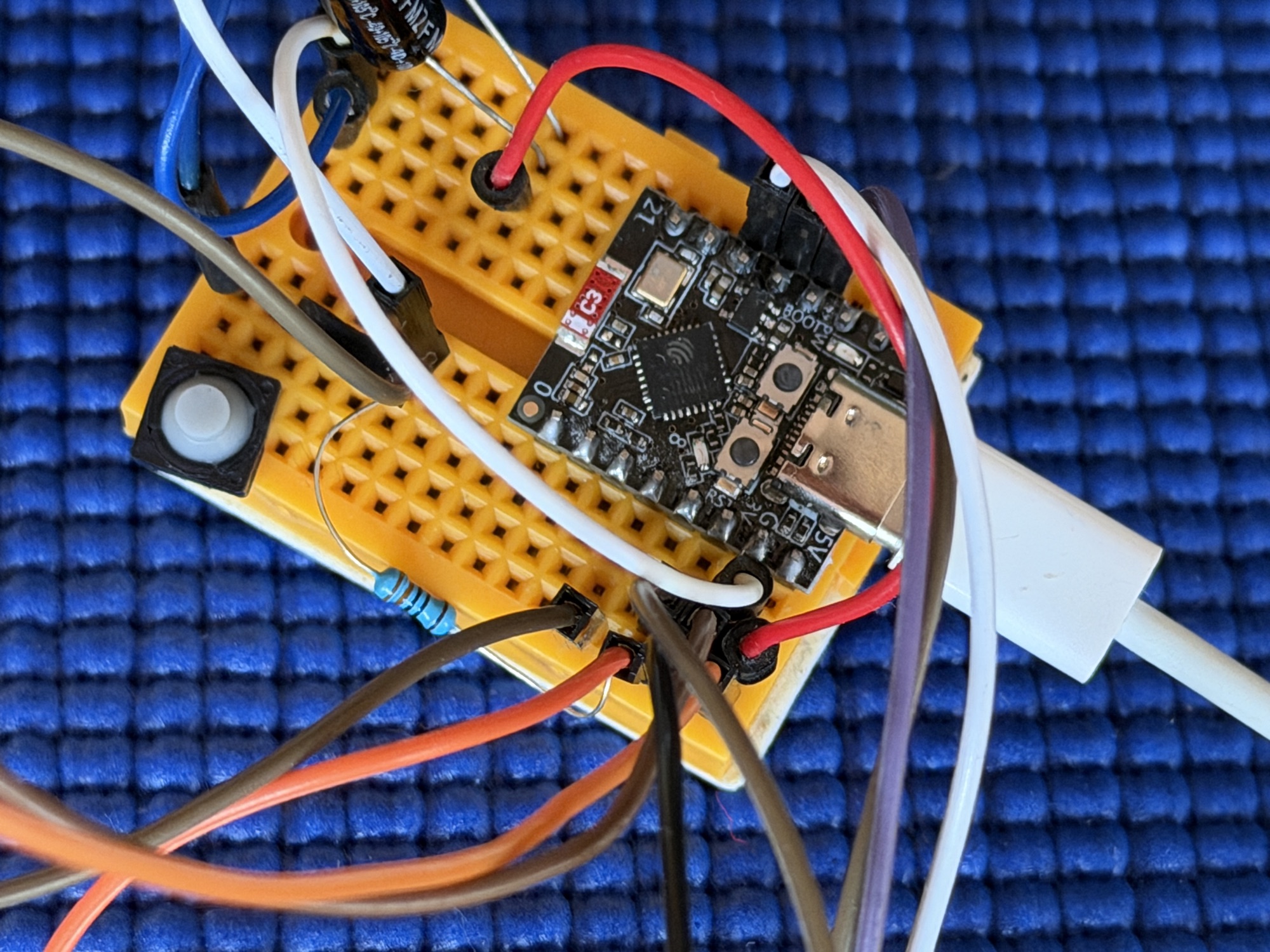 Nahaufnahme des Steckbretts: ein daumengroßer ESP32-C3-Mikrocontroller mit USB-C-Anschluss, ein Taster, ein Widerstand und ein Knäuel bunter Drähte.