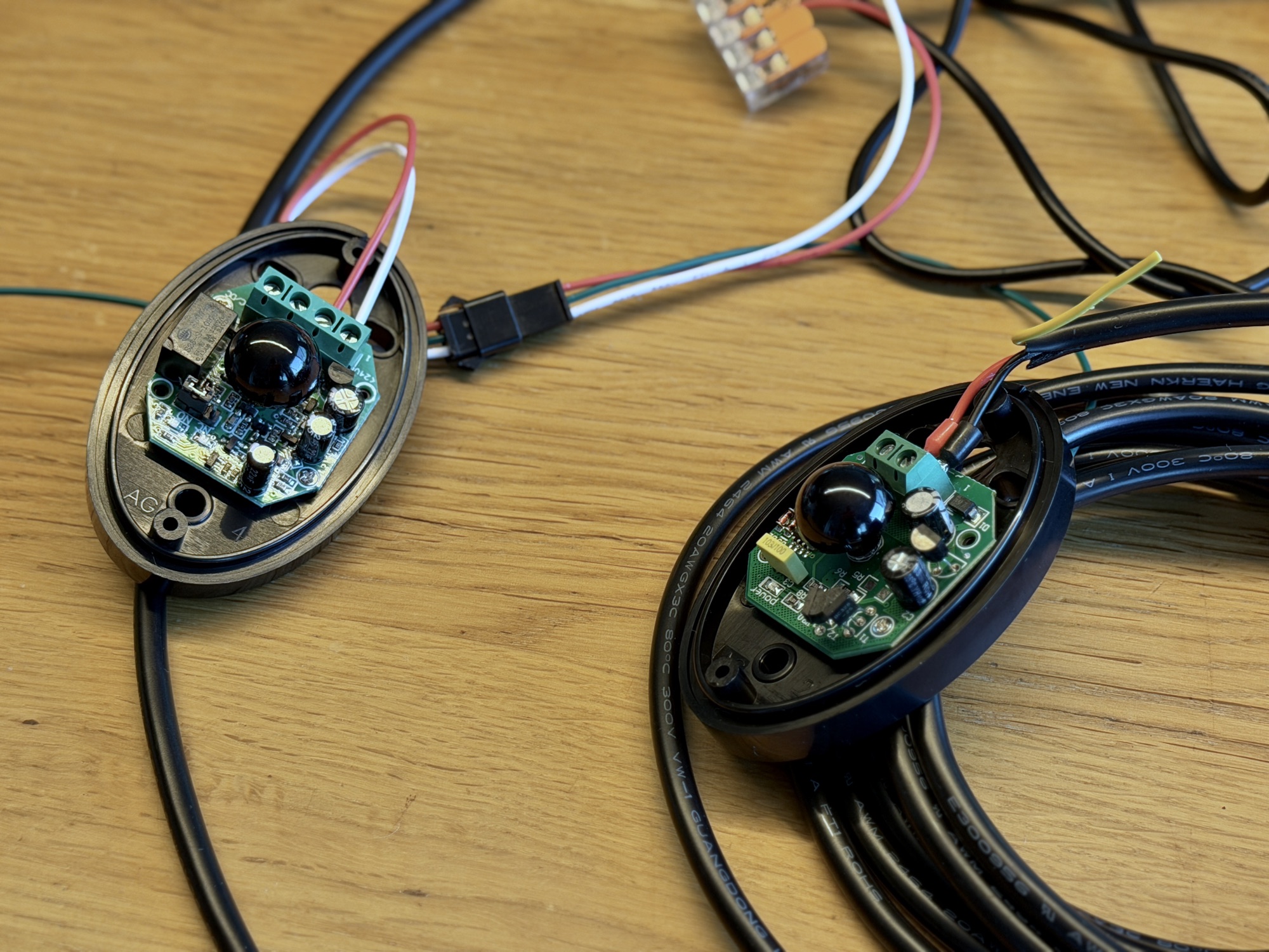 Zwei ovale Infrarot-Sensormodule auf einem Holztisch, verbunden mit Kabeln – Sender und Empfänger einer klassischen Lichtschranke.