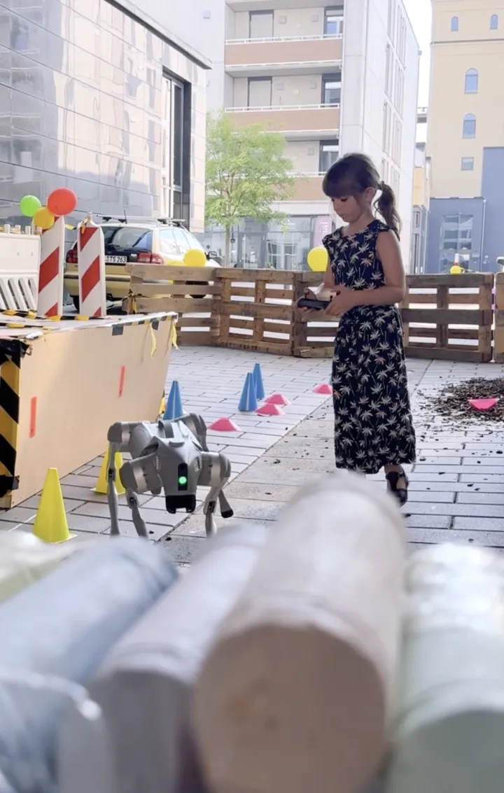 Ein Kind steuert den Roboterhund über einen Parcours aus Pylonen im Innenhof.