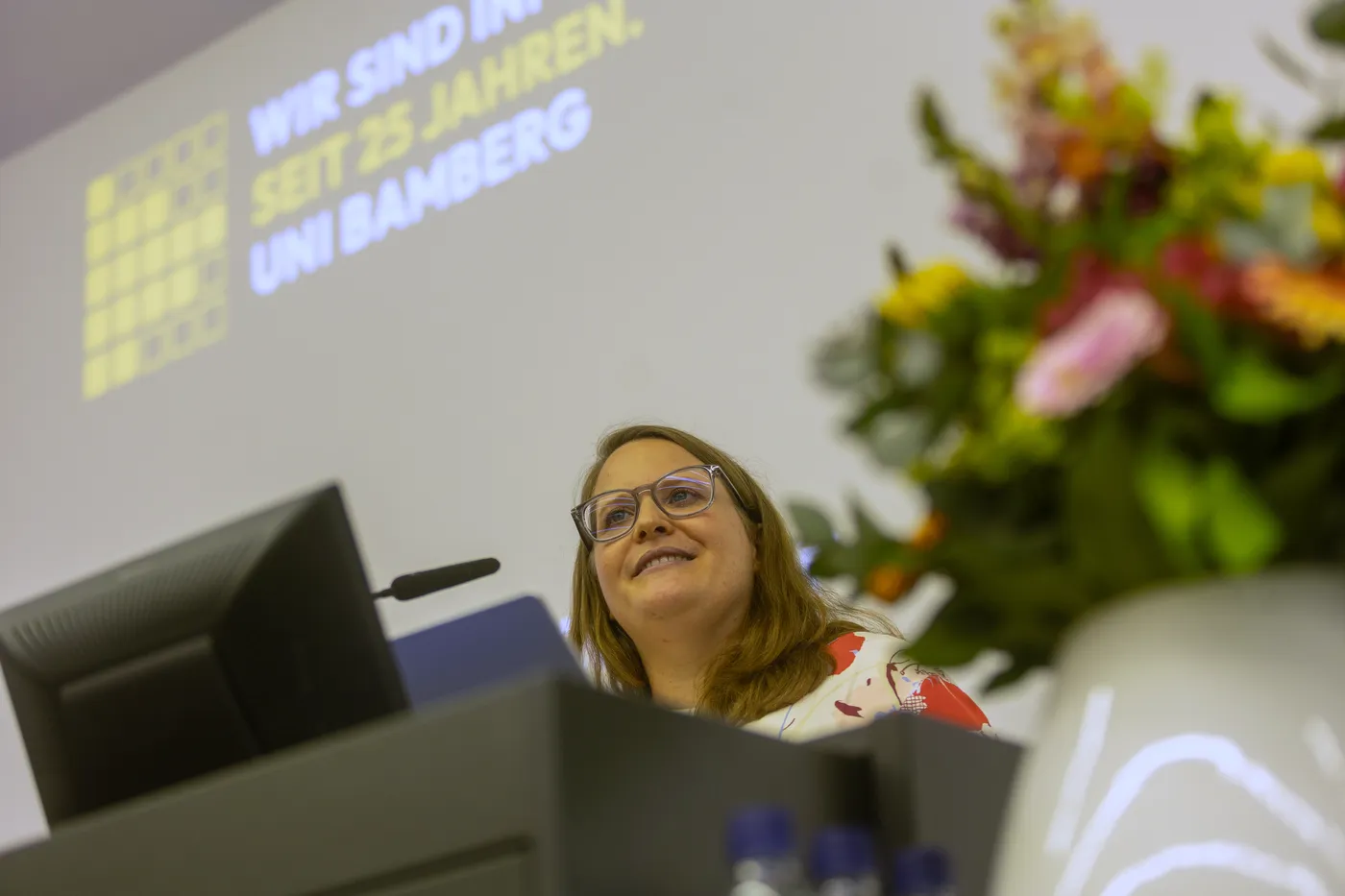 Dr. Anna Wiesinger lacht am Rednerpult, dahinter die Folie „Wir sind Informatik. Seit 25 Jahren. Uni Bamberg.“