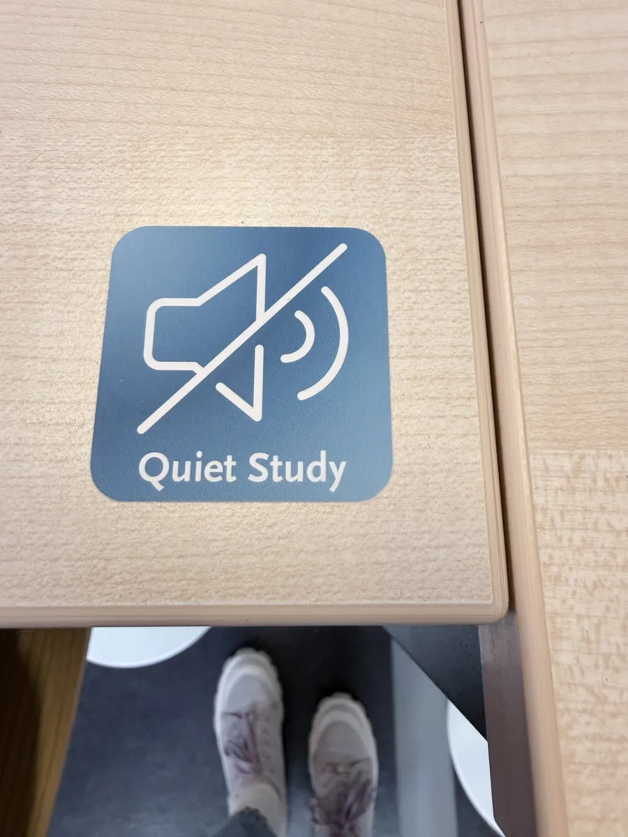 Schild mit durchgestrichenem Lautsprecher-Symbol und der Aufschrift Quiet Study auf einem hellen Holztisch